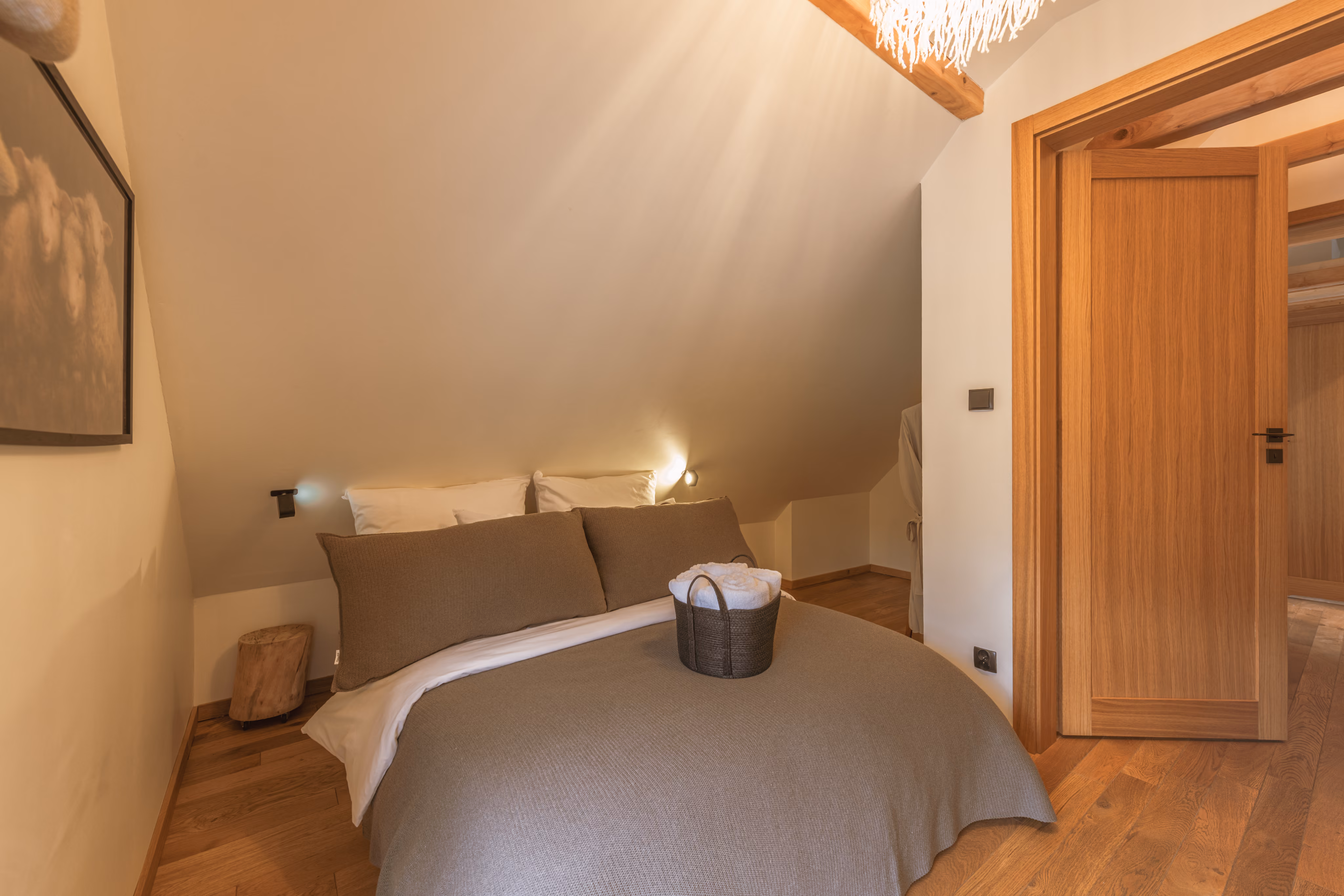 Cozy bedroom with sloped ceiling, double bed with brown bedding, and wooden door open to hallway.