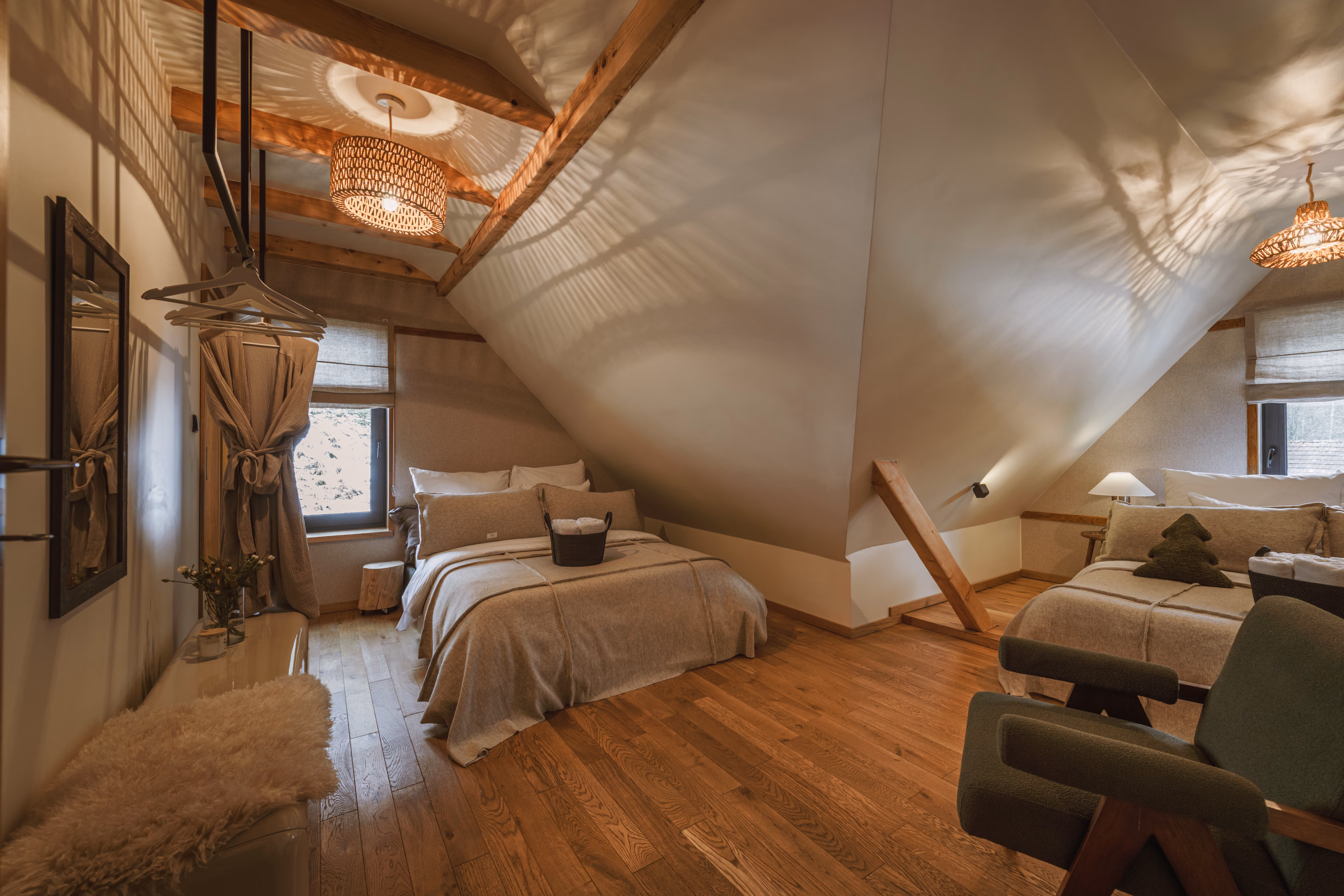 Cozy attic bedroom with wooden floors, two beds, lamps, and a green armchair.