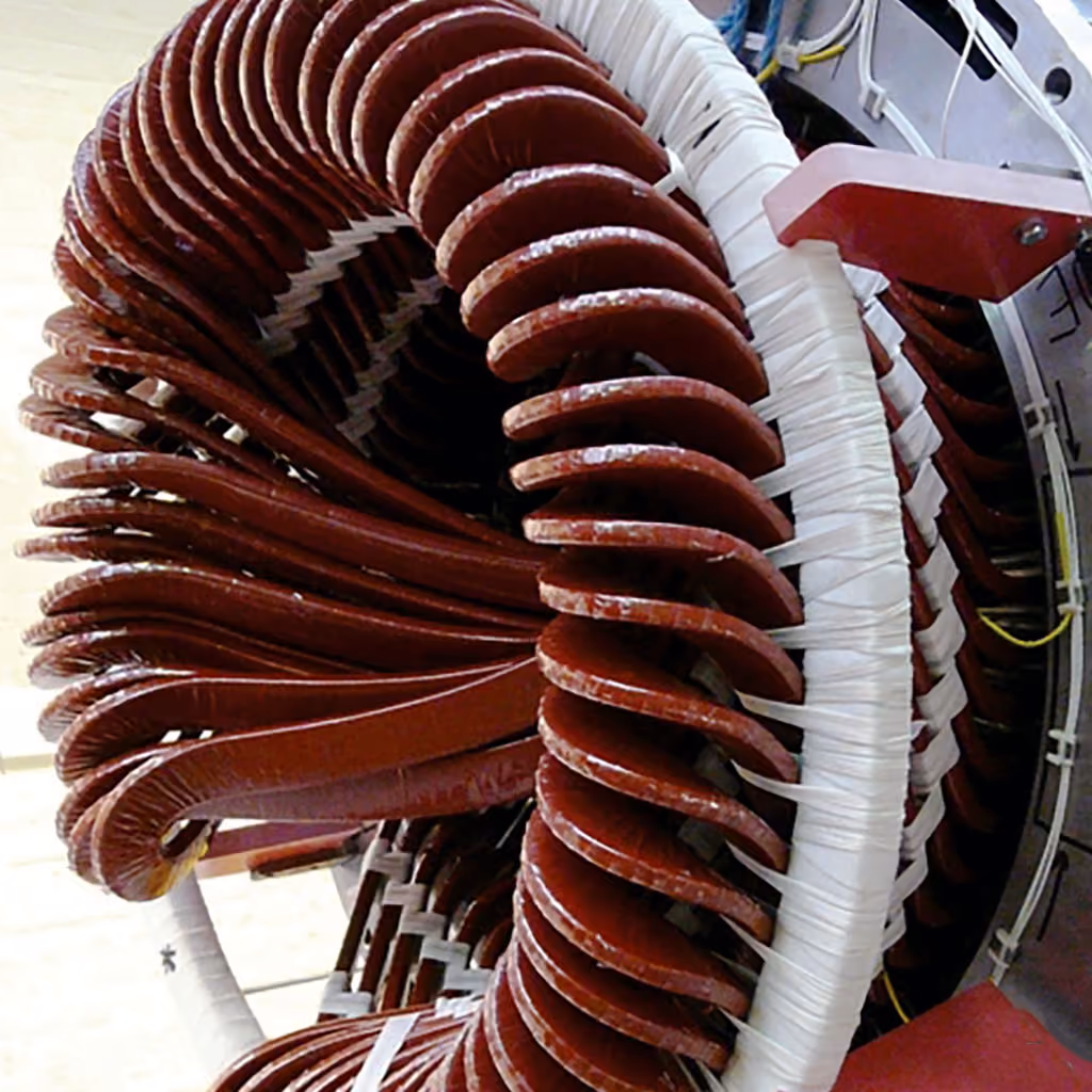 Close-up of a complex coil winding with insulated copper wire loops wrapped around a white circular core in an electrical machine component.