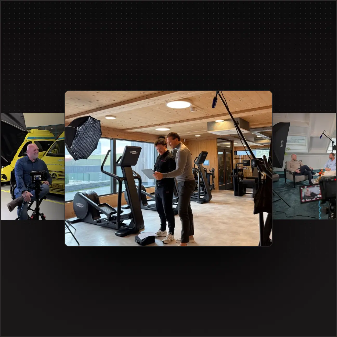 Two men in gym looking at a tablet with exercise machines and filming lights around them.