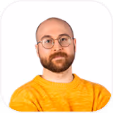 Man with glasses, bald head, and beard wearing a mustard yellow sweater against white background.