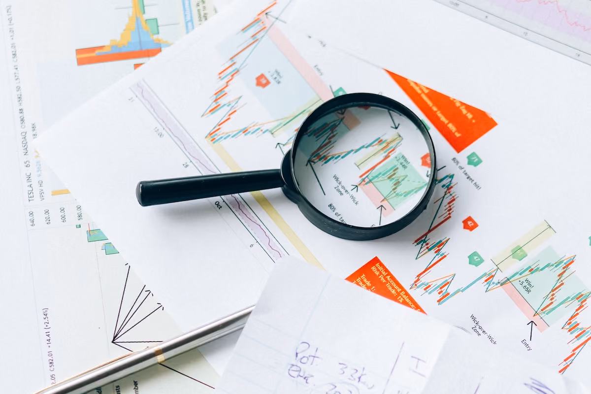 Financial documents and charts with a magnifying glass, symbolizing analysis and data review.