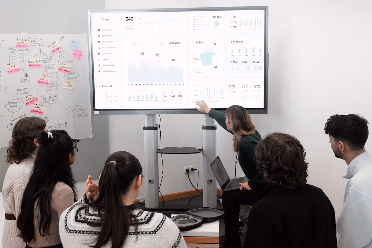 Group of professionals engaged in a business presentation examining charts on a large screen.