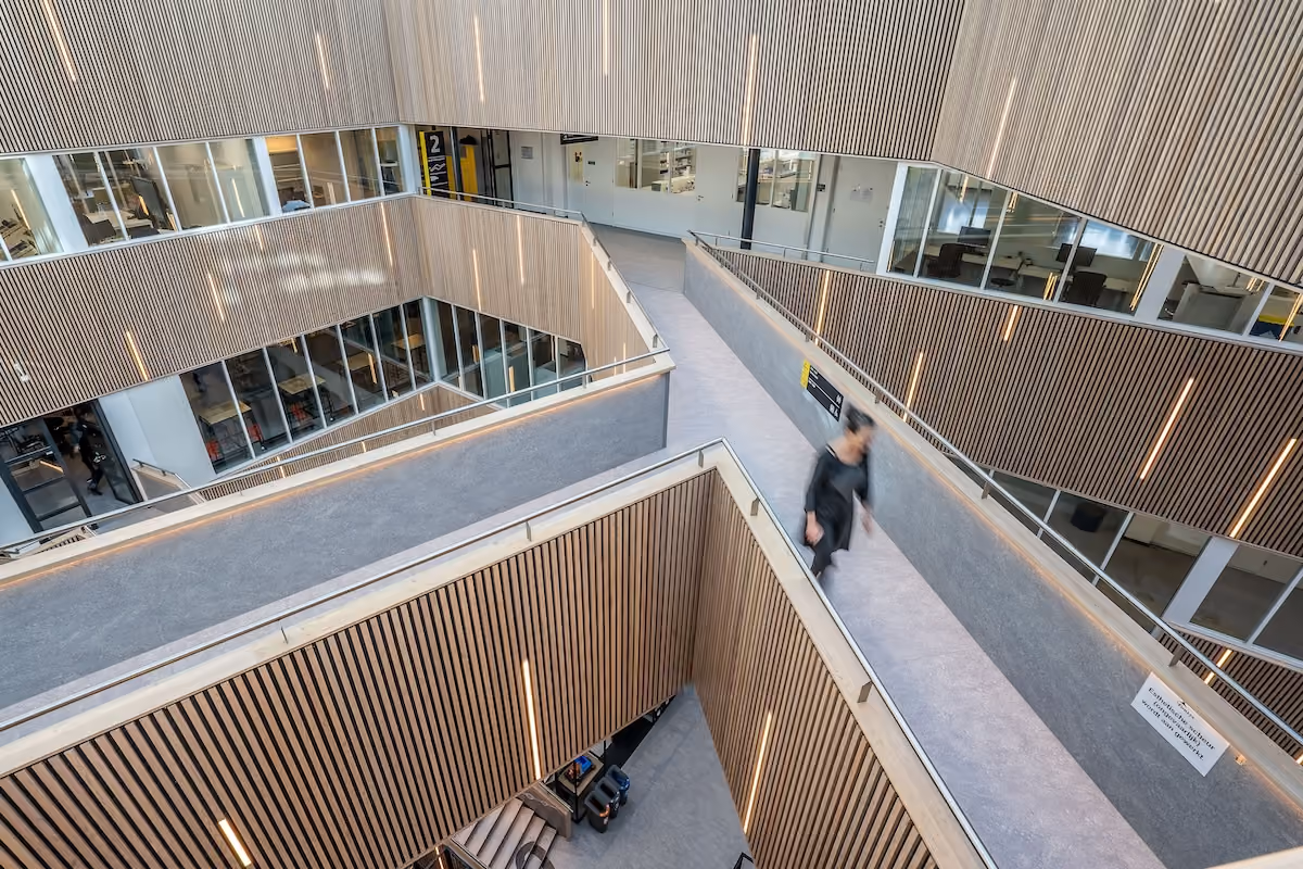 A person walks through a contemporary building interior with wooden slat design and angular walkways.