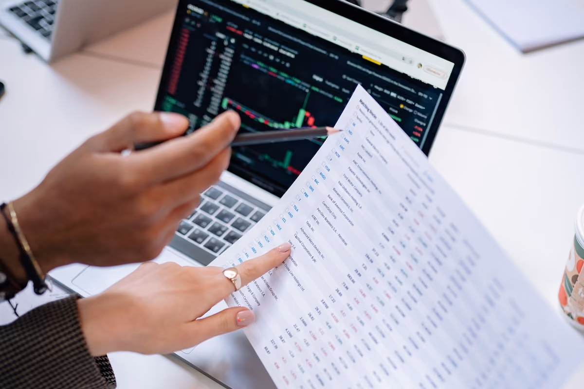 Hands holding documents analyzing data on a laptop in a collaborative office setting.