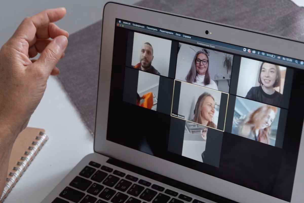 Hands at a laptop showing a group video call in a home office setting.