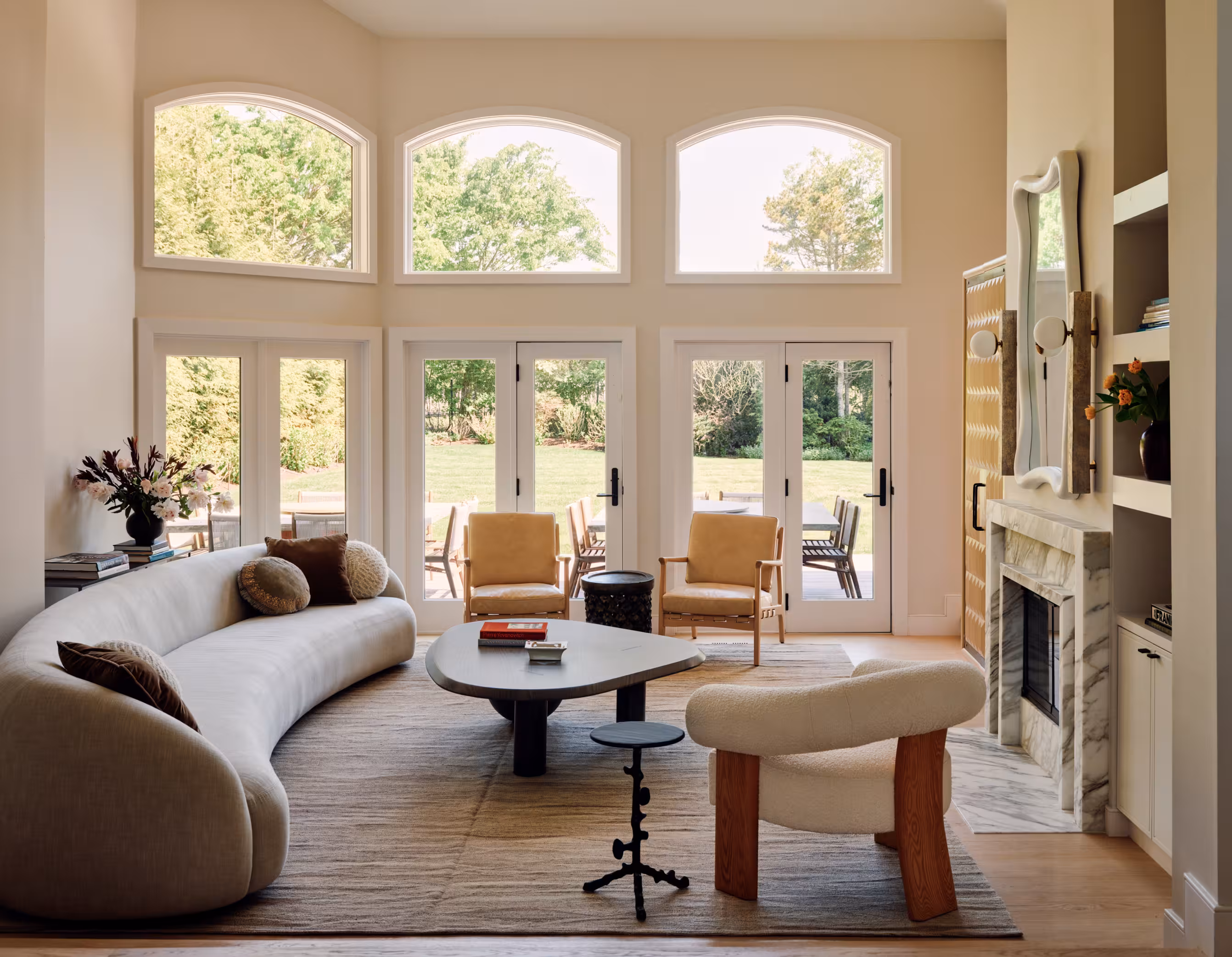 A living room with a curved sofa, a round coffee table, and arched French doors opening to the garden.
