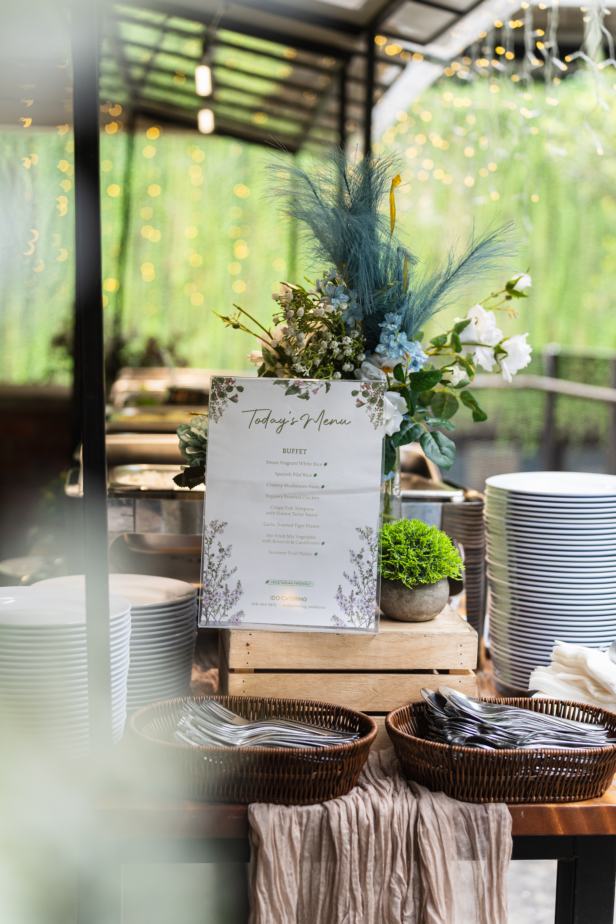 Buffet table set in a garden glasshouse, lit by daylight and string lights