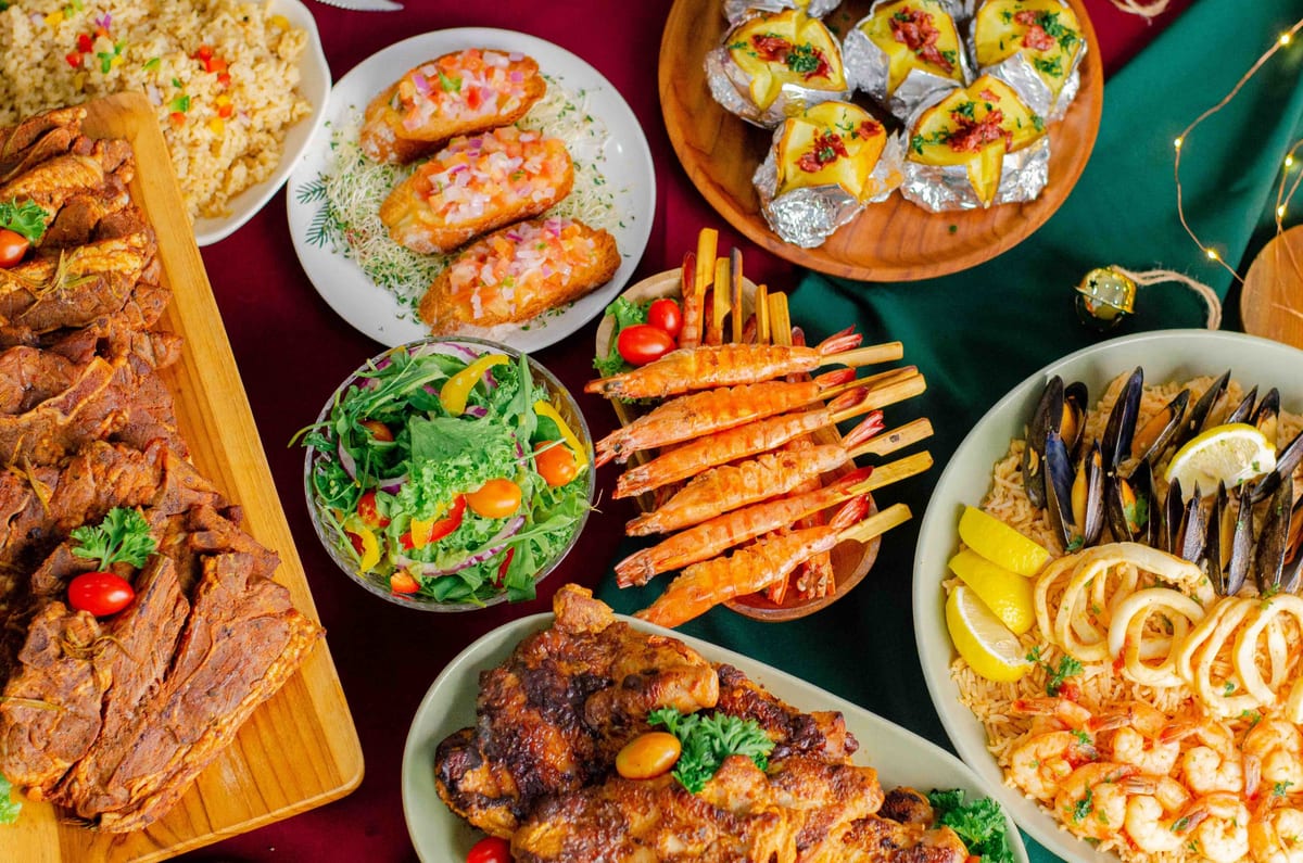 Flat lay of iDoCatering Christmas 2021 menu — grilled lamb, prawn skewers, baked potatoes, salad and seafood rice