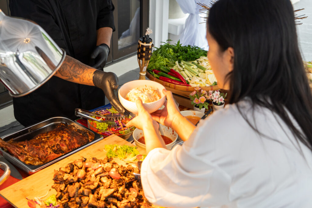 Chef serving guests at a live station with roast lamb, grilled chicken and ulam platter, Hari Raya 2024 catering