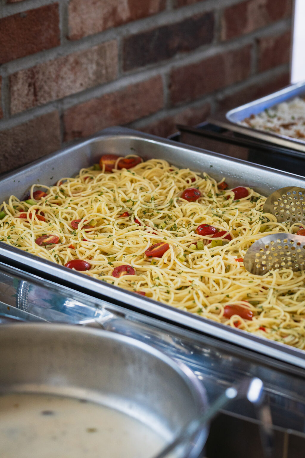 Chafing tray of aglio olio spaghetti with cherry tomatoes at an annual dinner buffet catered by iDoCatering
