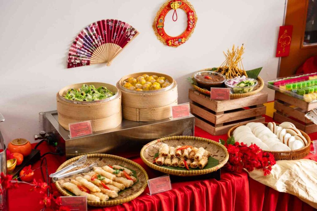 CNY table with bamboo steamers of dim sum, satay skewers, fried rolls, steamed buns and nyonya kuih by iDoCatering