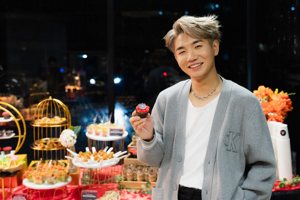 Guest KOL Chang Le smiling brightly showcasing red dessert cup cake from iDoCatering