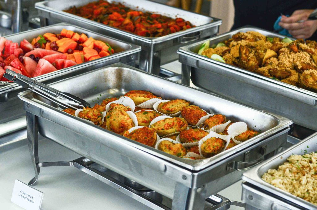 Chafing trays of cheesy herb loaded potato, fried chicken, fried rice and fruit at an office lunch buffet by iDoCatering