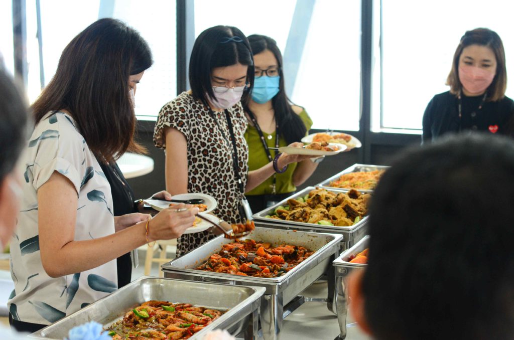 Guests wearing masks and getting food from silver trays at the office buffet catering by iDoCatering during 2022 COVID-19