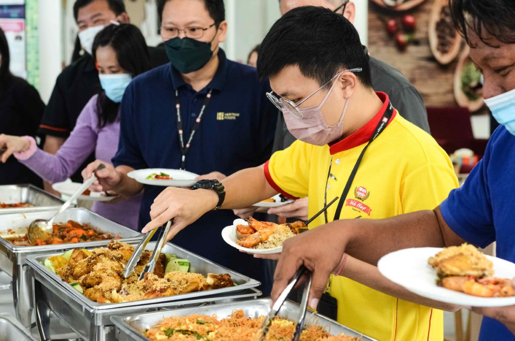 Yellow shirt guy wearing mask and getting food from silver trays at the office buffet catering by iDoCatering during 2022