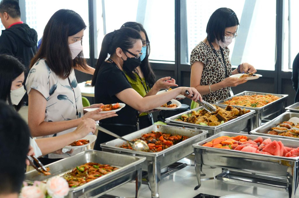 Guests wearing masks and getting food from silver trays at the office buffet catering by iDoCatering during 2022 COVID-19
