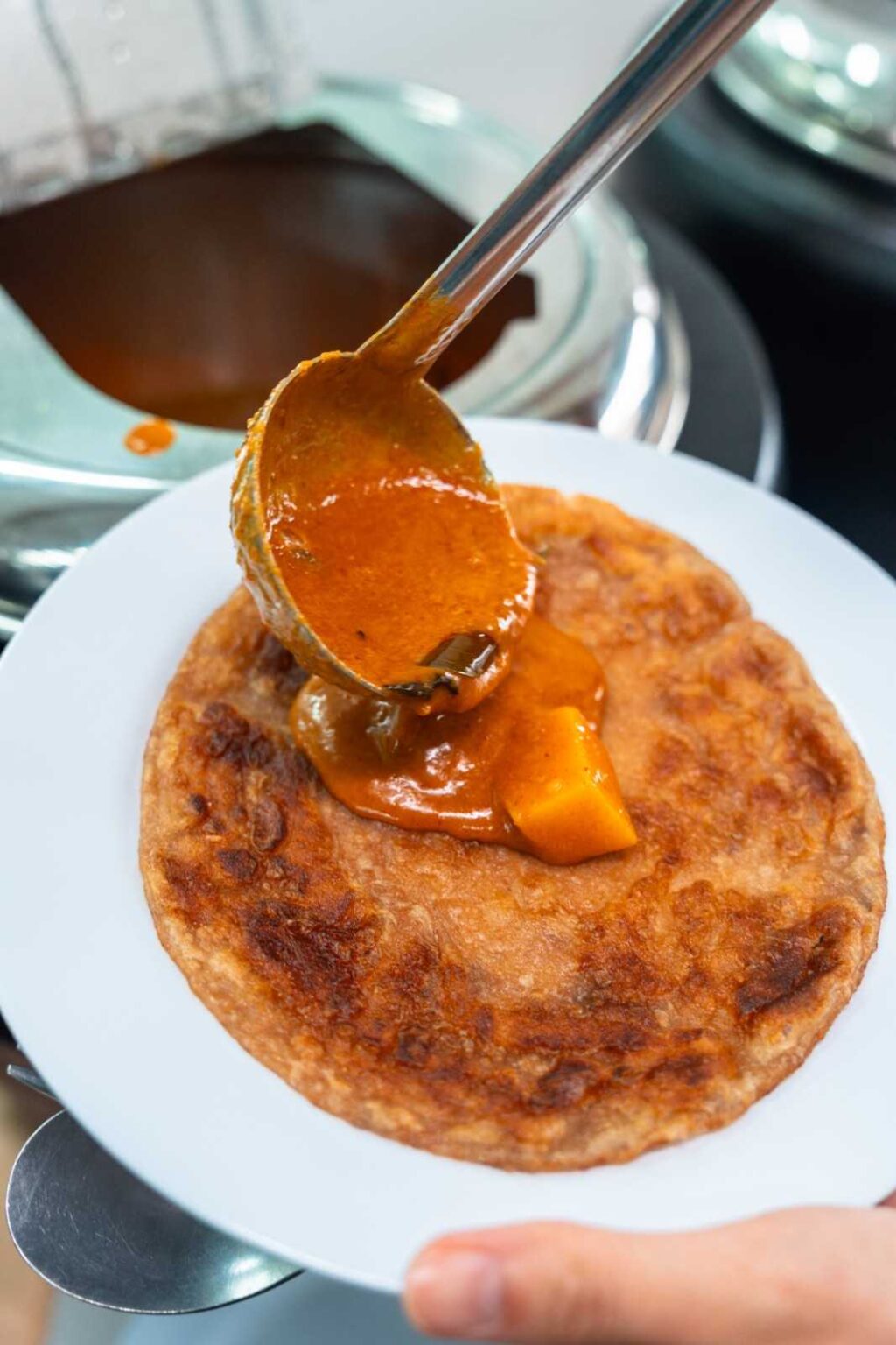 Ladle of potato curry poured over crispy paratha at an office Deepavali catering by iDoCatering