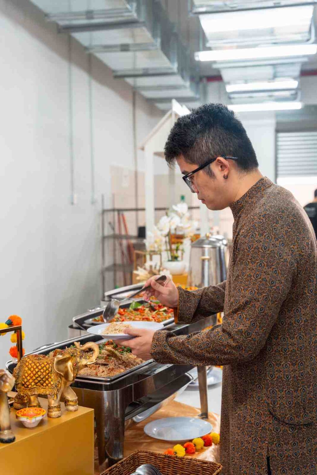 Guest in kurta serving rice at an office Deepavali buffet with elephant and diya decorations