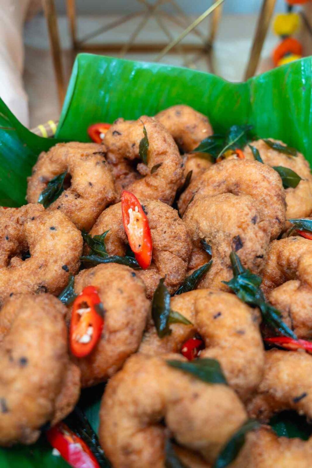 Crispy ulundu vadai with curry leaves and chilli on banana leaf at an office Deepavali catering