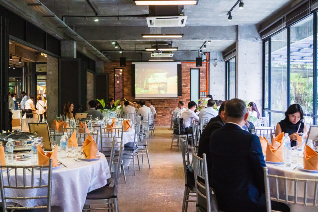 Guests at round banquet tables facing a projector screen at a corporate event catered by iDoCatering
