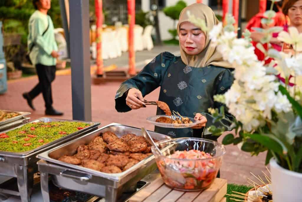 Guest serving fried patties at an iDoCatering Hari Raya buffet with herbed rice and kerabu salad