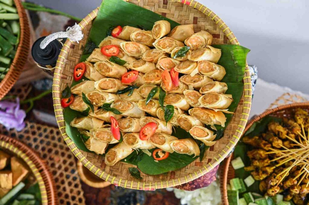 Mini popiah rolls with red chilli slices on banana leaf in a rattan tray, iDoCatering Hari Raya catering
