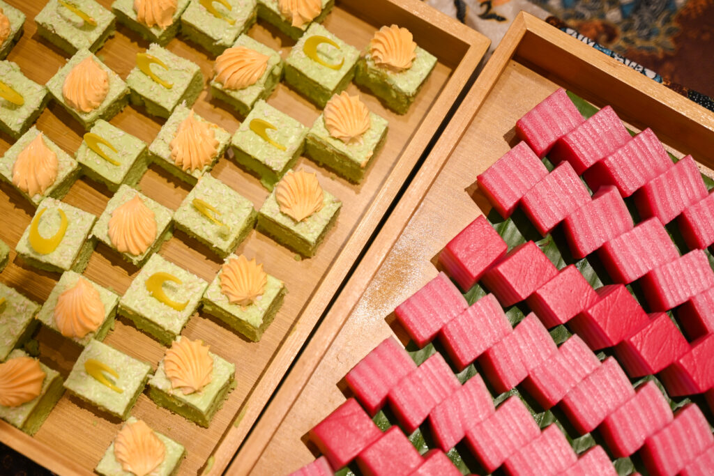 Wooden trays of pandan cake squares and pink kuih cubes, iDoCatering Hari Raya dessert spread at Mercu UEM