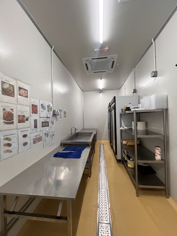 Canape room at iDoCatering, its wall lined with laminated dish spec sheets above a stainless prep bench and shelving