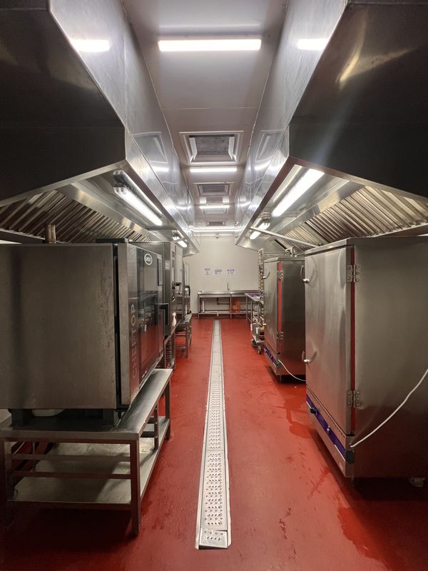 Bake room at iDoCatering with combi ovens either side of a red epoxy aisle, extraction hoods and a floor drainage channel