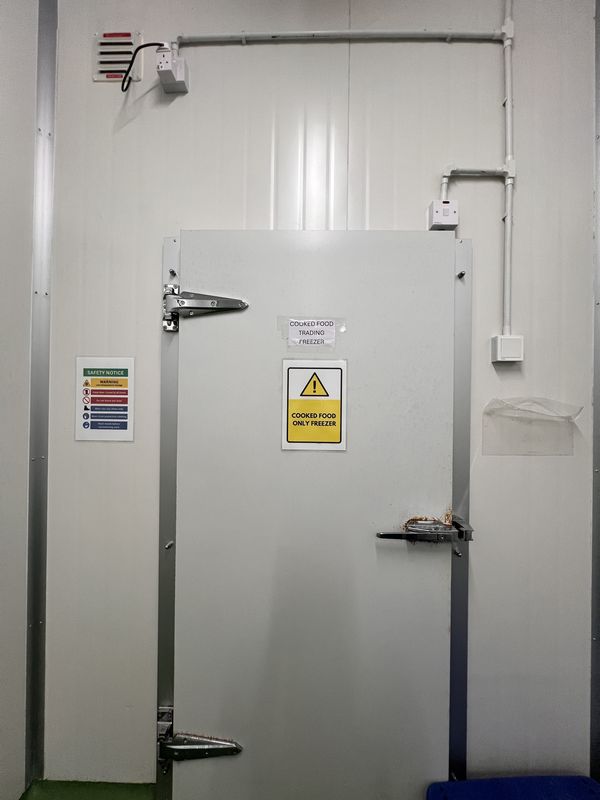 Walk-in freezer in iDoCatering's kitchen, labelled for cooked food only, with overhead pipework and a hygiene chart