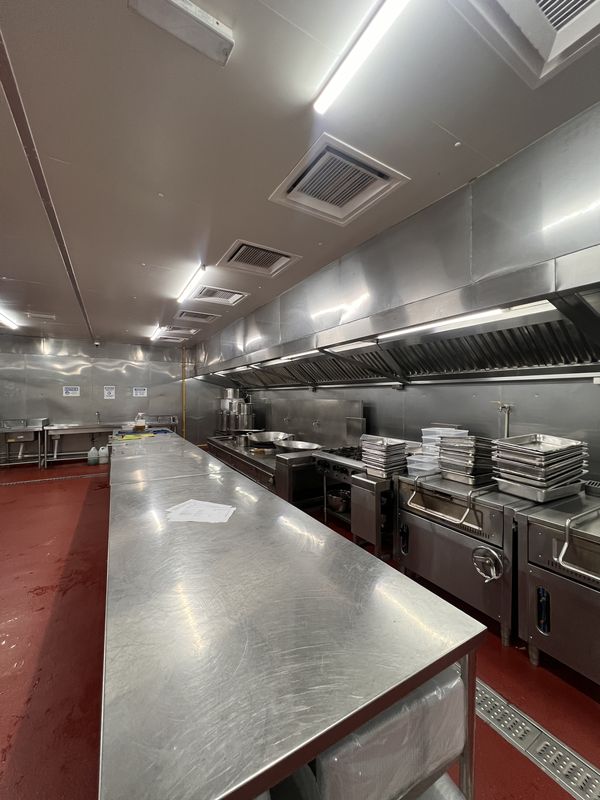Cook room at iDoCatering: long stainless prep table beside the range line, stacked gastronorm trays, red epoxy floor
