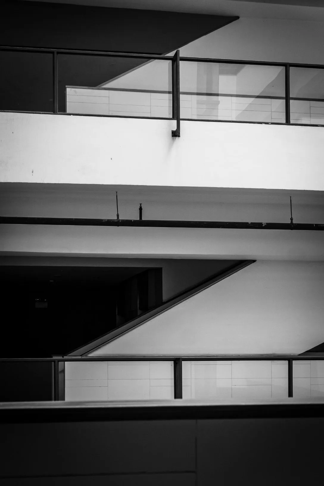 Black and white photo of geometric architectural features of a building interior with railings and stairway.