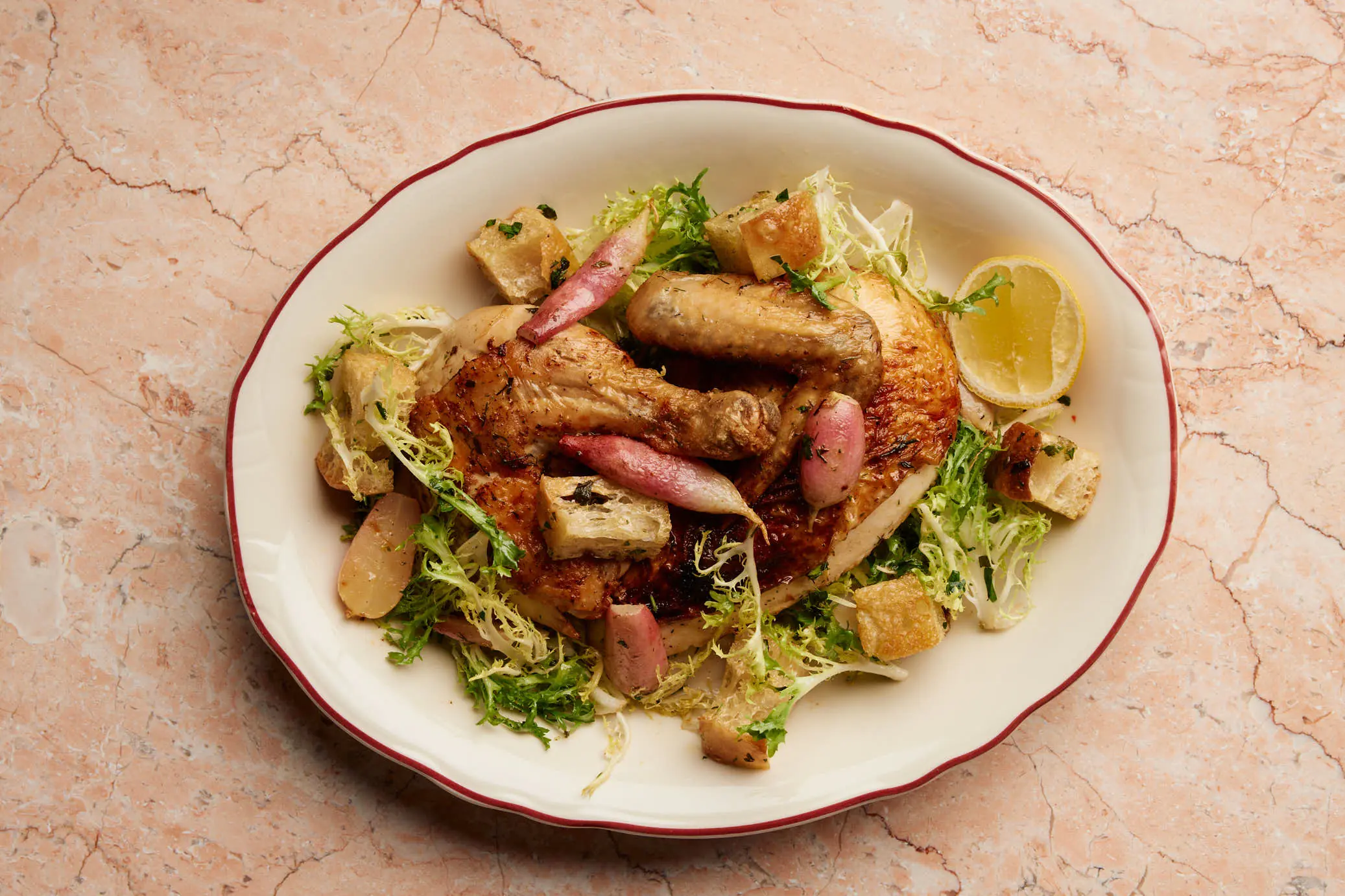 A frisee salad with croutons and cured meat on a rimmed plate