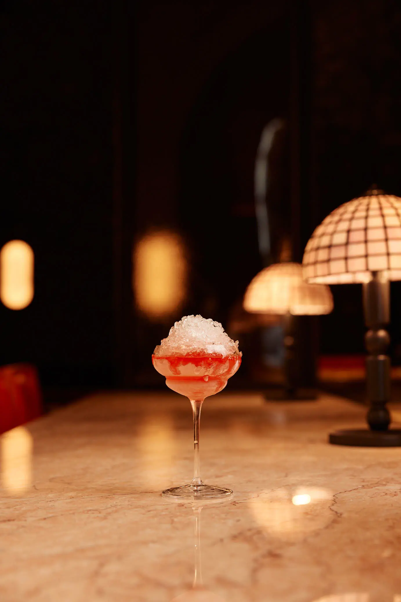A coupe cocktail lit by a table lamp in the dining room