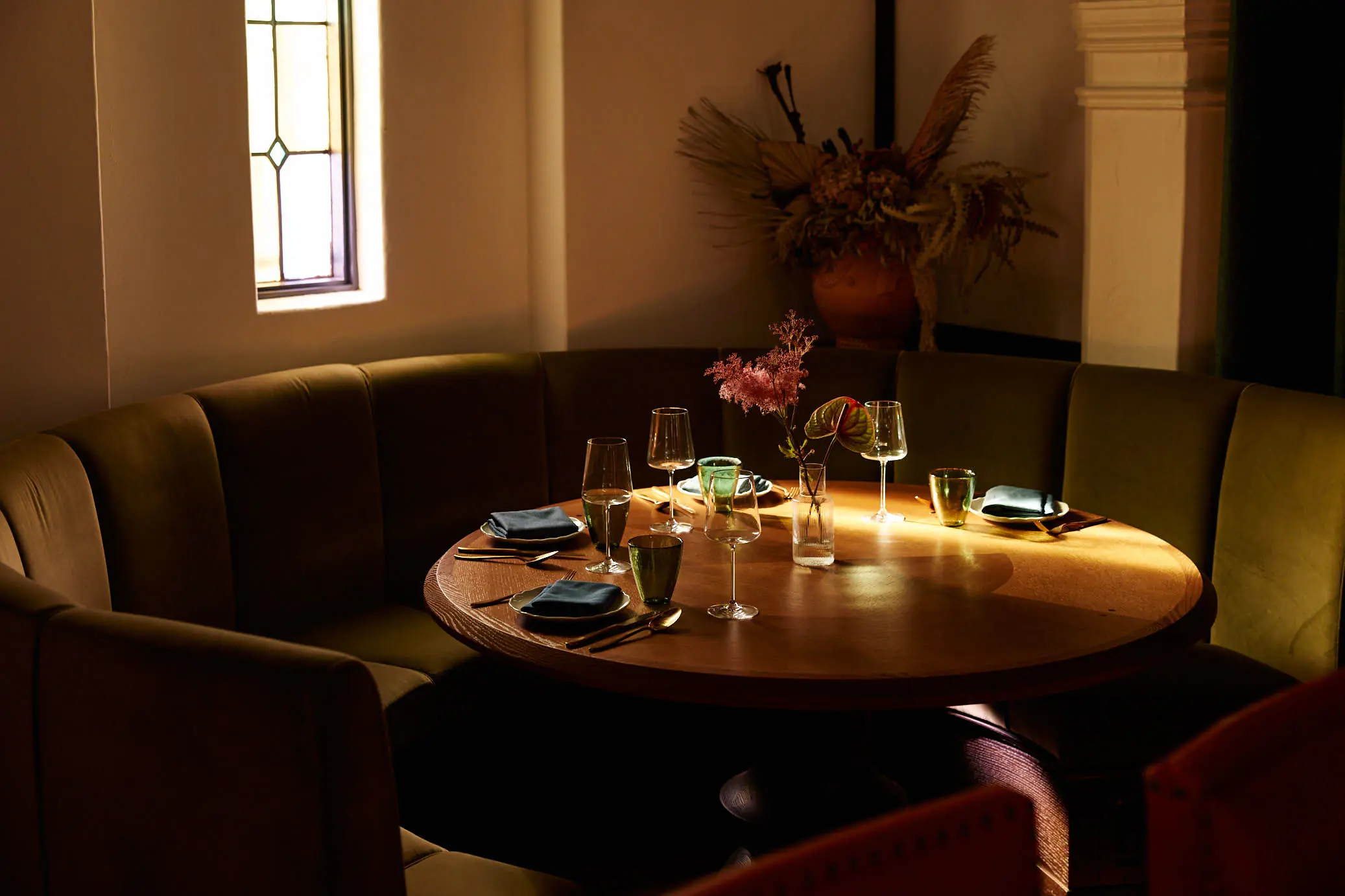 A curved banquette set for dinner with flowers and low light