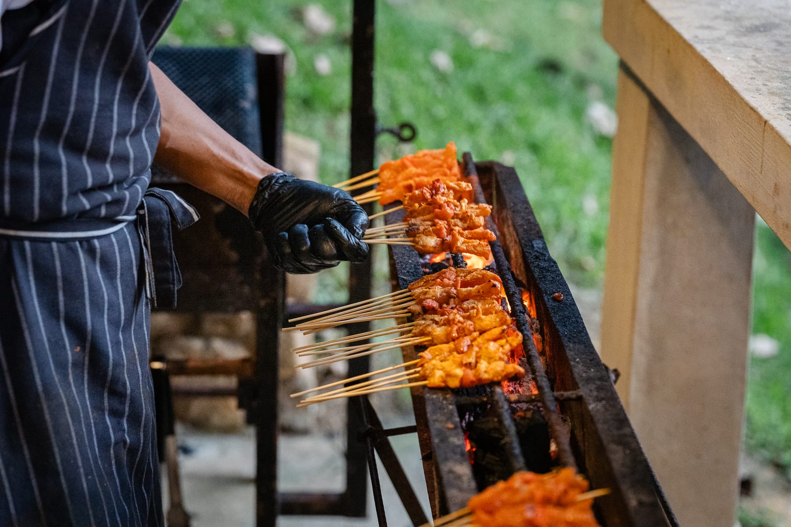 Chef grilling chicken satay over charcoal at a garden wedding live station — iDoCatering