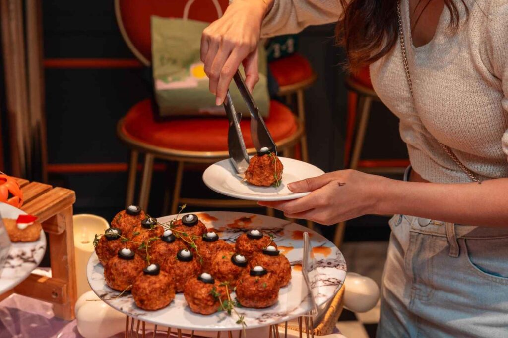 Guest picking a Zombie Eye meatball with tongs at the Paxtonz Halloween party at Empire City