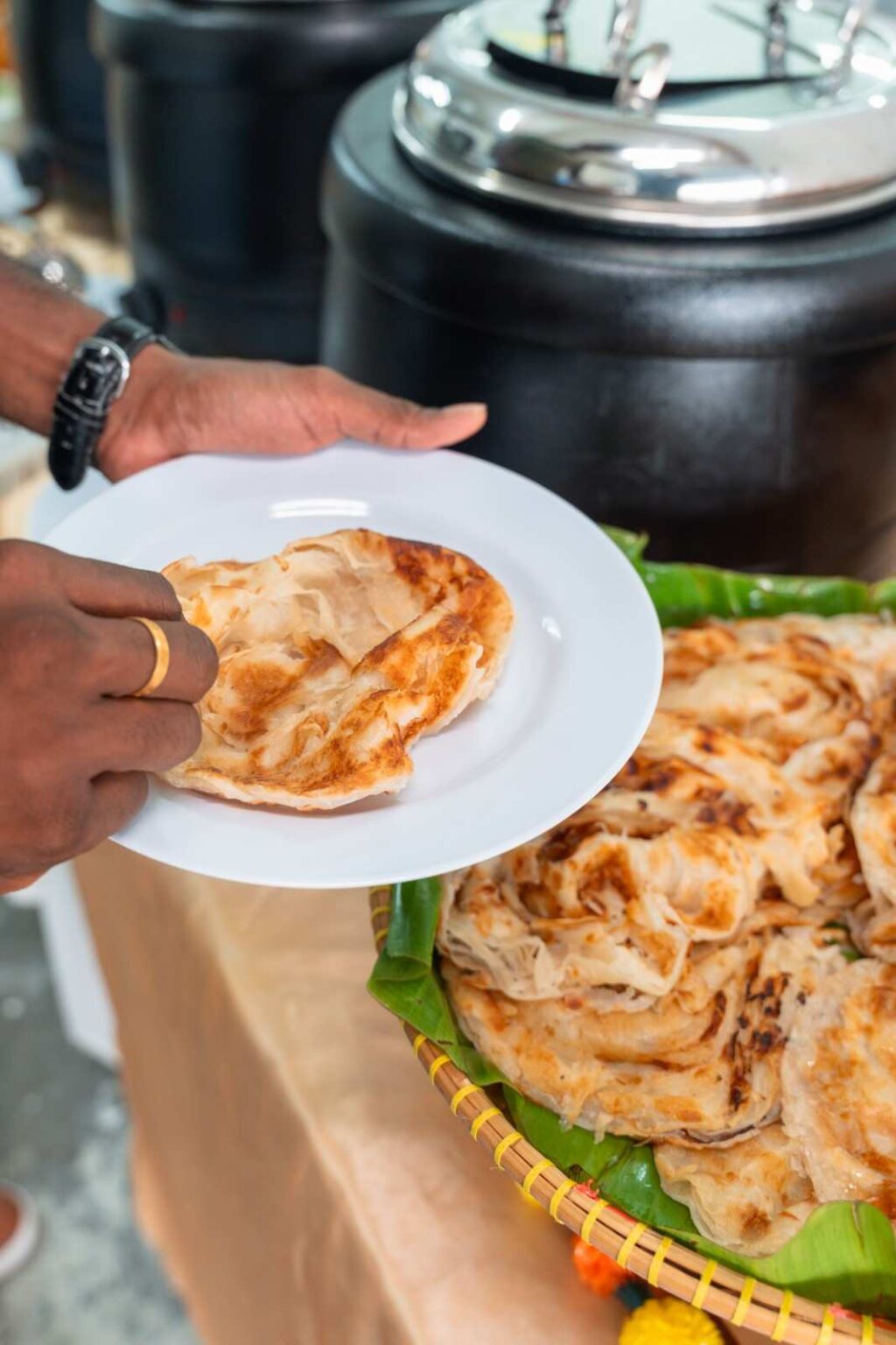 Guest plating roti canai from a banana-leaf basket at an office Deepavali buffet by iDoCatering
