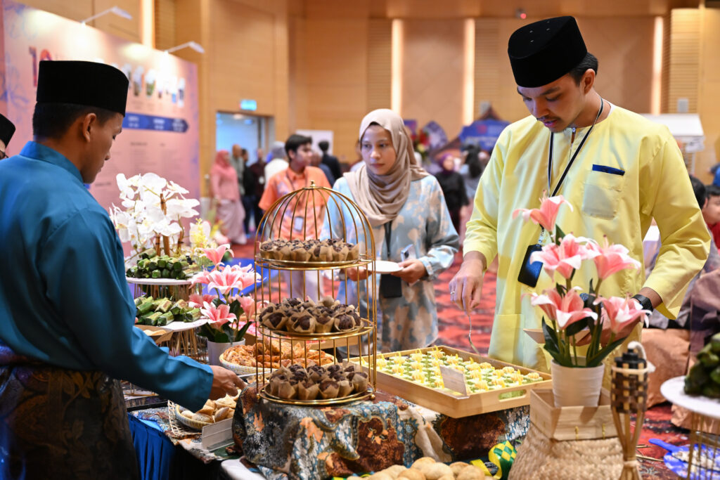 Guests in baju Melayu at a kuih dessert table with birdcage stands, Hari Raya corporate event at Mercu UEM