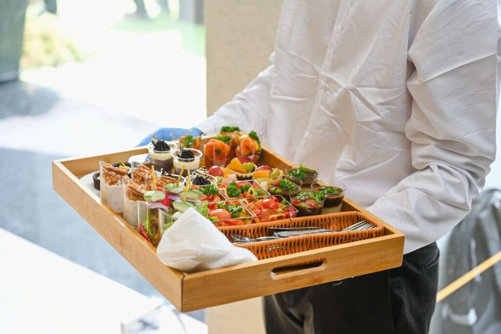iDoCatering server presenting a wooden tray of canapé cups and desserts at a corporate launch in KL