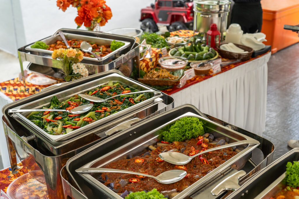 Chafing dishes of sambal eggplant and stir-fried greens on an iDoCatering Malay wedding buffet line under a marquee