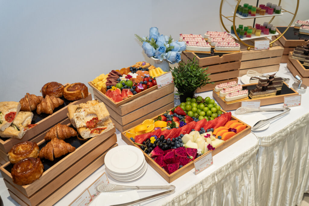 Grazing table of croissants, focaccia, fruit platters and petit cakes in wooden crates - iDoCatering