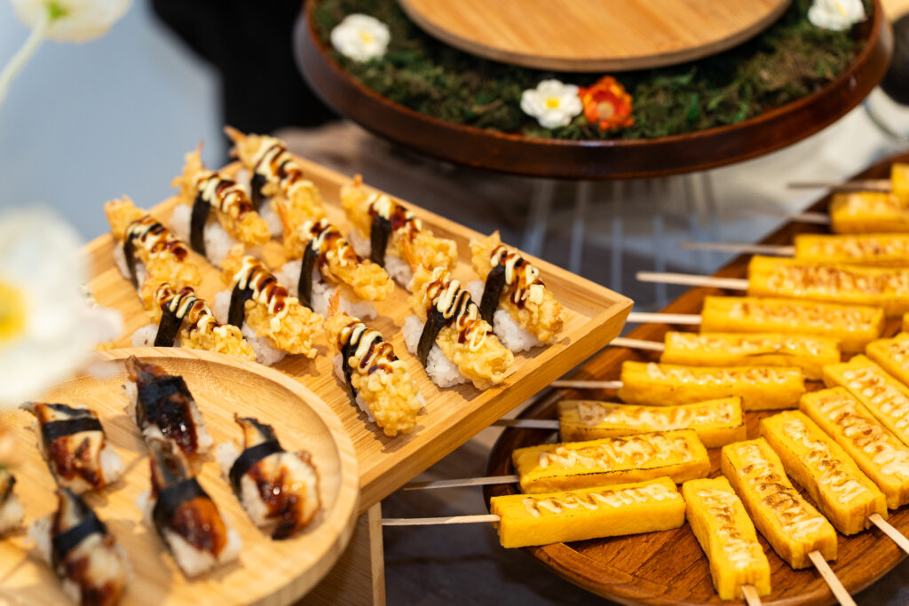 Japanese live station of tempura nigiri, unagi sushi and tamago skewers on wooden boards - iDoCatering