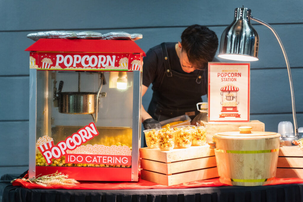 iDoCatering-branded popcorn machine and buttery popcorn cups at a corporate event popcorn station