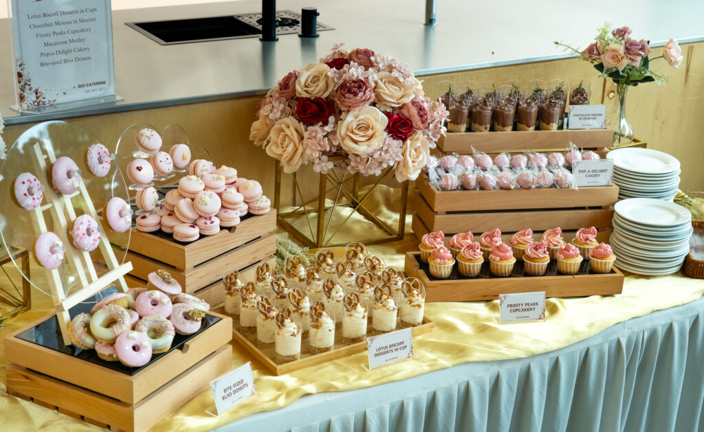 iDoCatering dessert table of macarons, glazed donuts, cupcakes and biscoff dessert cups on tiered wooden stands