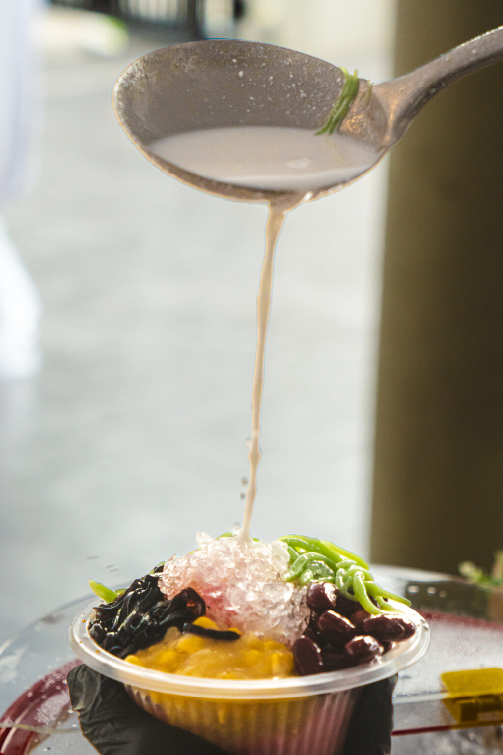 Coconut milk ladled over a bowl of cendol with red beans and sweet corn at an iDoCatering Hari Raya dessert station