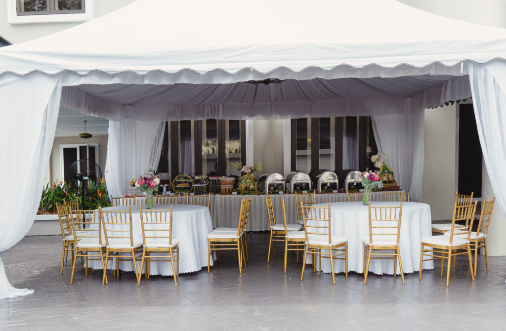 White marquee with gold chiavari chairs and an iDoCatering buffet line of chafing dishes at a Hari Raya open house