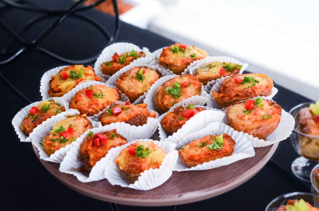 Cheese-topped potato croquettes in paper cases on a wooden stand, iDoCatering launch event bites