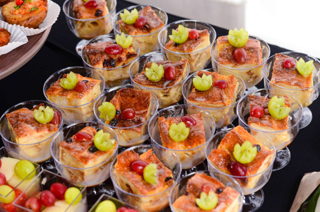 Bread pudding squares in clear cups topped with grapes and starfruit - iDoCatering finger food catering